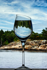 A glass goblet with clear water against the backdrop of the island's rocky shore