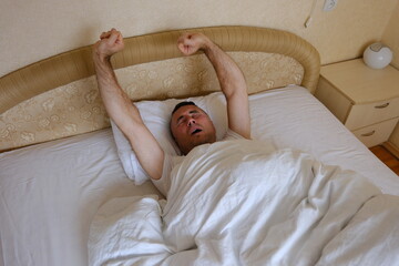 man stretching on bed in cozy bedroom with soft lighting and minimalistic decor featuring books and a small lamp. High quality photo