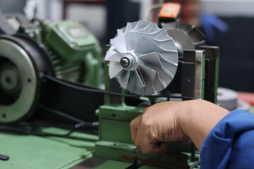 Technician hands adjusting a turbocharger compressor wheel on a dynamic balancing machine, precision mechanical engineering and maintenance process in a workshop.