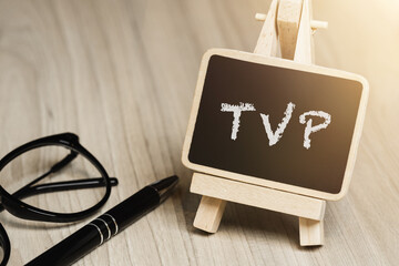 Black writing board on a wooden frame with the inscription "TVP", next to black glasses and a pen (selective focus)