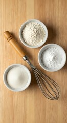 Top view of baking ingredients including flour and sugar in bowls with a wire whisk on a wooden board. Kitchen food preparation flat lay.