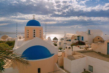 Traditional blue domed church in Oia village on Santorini island, Greece, overlooking the Aegean Sea under a cloudy sky.