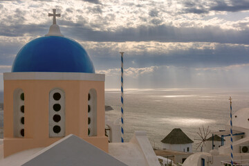 Traditional blue domed church in Oia village on Santorini island, Greece, overlooking the Aegean Sea under a cloudy sky.