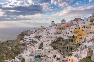 Panoramic view of whitewashed cliffside houses and windmills in Oia village on Santorini island, Greece, overlooking the Aegean Sea.