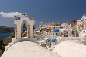 White bell tower and blue domed churches in Oia village on Santorini island, Greece, overlooking the caldera and sea.