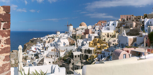 View of traditional windmill and domed church by the sea in Oia village on Santorini island, Greece.