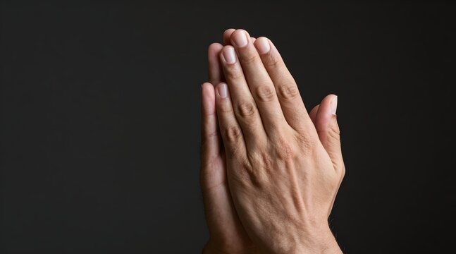 Two hands are clasped together in a posture of prayer against a dark background