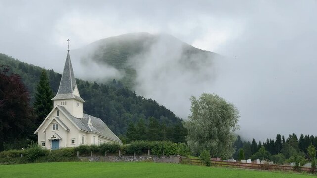 White wooden church surrounded by fog and mountains in norway