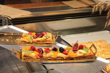 Colorful fruit tart slices with layers of puff pastry, custard and assorted fresh fruits displayed...