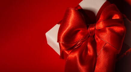 White Gift Box wrapped with a luxurious red satin bow on Red Background. Festive holiday composition symbolizing love, celebration, surprise, and special occasions, with copy space for text.