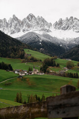 Idyllic alpine village nestled in green rolling hills below snow-capped mountains