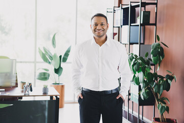 Confident businessman stands in modern office with plants and bookshelves in a bright loft style © deagreez
