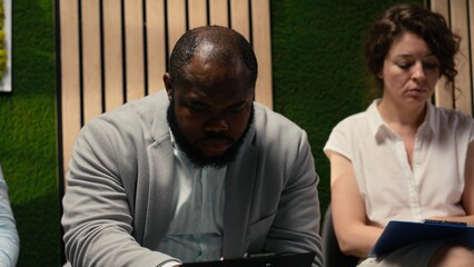 African american anxious male candidate reading his speech sitting in queue in the hallway, presenting his qualifications on the CV. Preparing for the selection and hiring process.