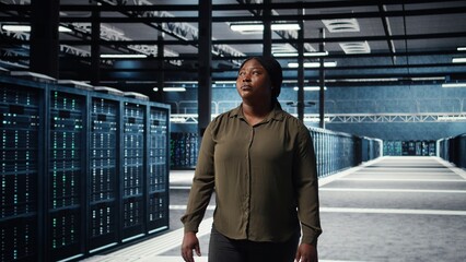 Fototapeta premium Portrait of cheerful data center engineer conducting security audits to protect against cyber threats. Jolly worker walking in server room, ensuring compliance with industry standards, camera A
