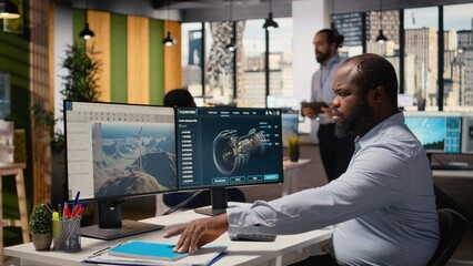 Technician working on wind turbine simulation in office, doing upgrades. African american man in RD department using CAD software on computer, doing renewable energy windmill engineering, camera A