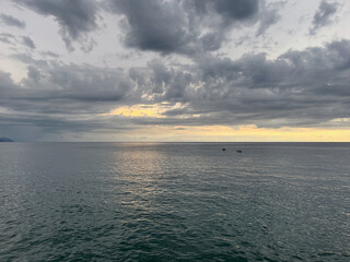  Dramatic sunset over calm ocean with dark storm clouds and golden light on horizon