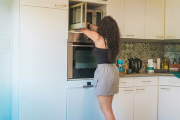 Middle-aged woman in her kitchen baking, she is opening the oven