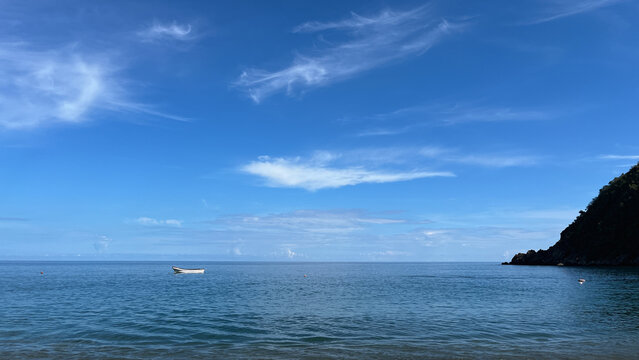 Small white boat floating on a calm blue sea with wispy clouds, mountains, and a tropical coastline