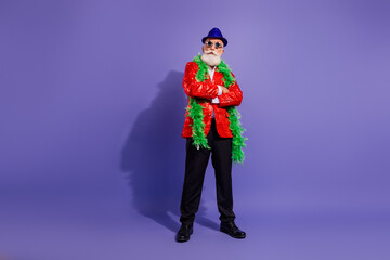 Charismatic male performer in red sequined jacket with green boa and blue hat posing for party and holiday show against purple background