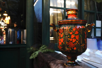 Traditional black russian tea samovar with bright floral painted ornament standing on fur counter at winter fair