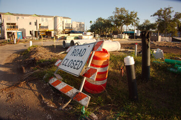 A bustling Construction Site With Road Closed Signage And Utilities On A Work Zone. Orange barrels...