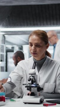 Vertical video Hematology specialist in lab analyzing batch of blood samples for red blood cell abnormalities. Technician doing research on sanguine fluid vials to diagnose anemia types, camera A