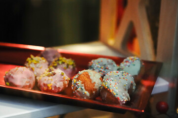 Assorted sweet glazed mini donuts topped with colorful sprinkles and crushed nuts arranged on red...