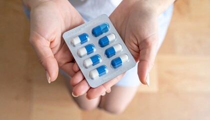 Close-up of a person&rsquo;s hands holding a blister pack of blue and white capsules, with one capsule resting on the palm. The image conveys themes of medication, health care, and pharmaceutical use.