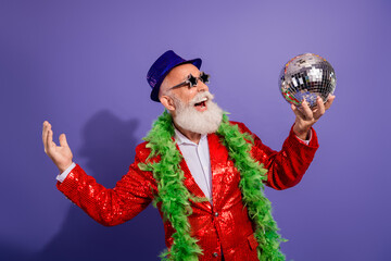 Energetic elderly man in red sequin jacket and green feather boa dances with a disco ball during a...