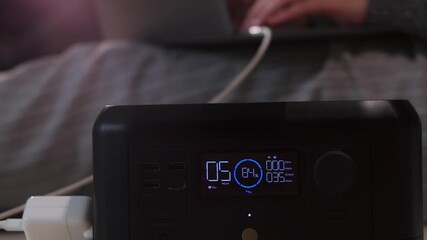 A portable power station is actively charging a laptop, displaying an 84% battery level and 35 watts output