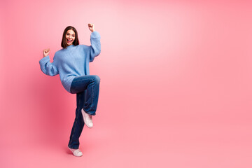 Young woman jumping in a blue sweater against a pink background for fashion lifestyle advertising...