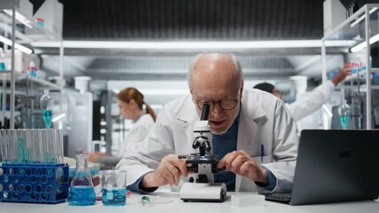 Portrait of cheerful senior lab researcher looking through scientific microscope lens to study cells. Elderly microscopist performing biological sample examination with optical equipment, camera A