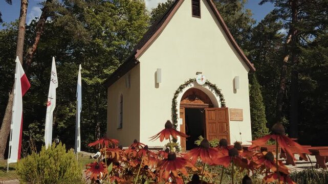 Sunny horizontal view of the "Sanktuarium Matki Bożej Trzykroć Przedziwnej" in Koszalin on Chełmska Mountain featuring rudbeckia flowers and the Polish flag