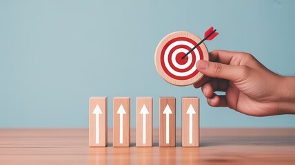 A hand holding a target with an arrow hitting the bullseye above a row of wooden blocks with upward arrows