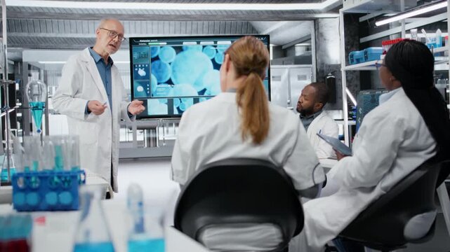 Senior scientist in lab presenting innovative DNA sequencing project to colleagues. Elderly team leader showing 3D biological model on screen to researchers during strategic briefing, camera B