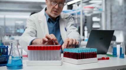 Senior scientist in lab analyzing batch of blood samples for red blood cell abnormalities. Elderly histology expert doing research on sanguine fluid vials to diagnose anemia types, camera B - Powered by Adobe