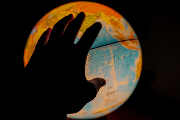 Illuminated Globe on Dark Background.Migration and politics.Moving to another country concept.Population migration.Political map of the world. Capture of territories.black hand silhouette on globe 