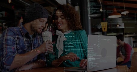 Leaning trio with beanie, plaid, teal jacket working on silver laptop at cafe showing code overlay