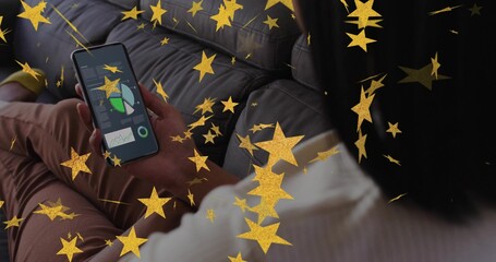 Holding phone, seated woman viewing charts on dark-gray sofa in white-ribbed-top, gold stars