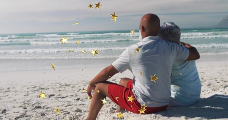 Sitting mature couple hugging facing ocean on white beach in summer clothes, gold stars, copy space