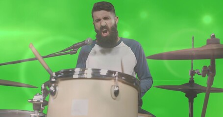 Singing bearded drummer playing drum kit in green screen studio, wearing raglan shirt with mic