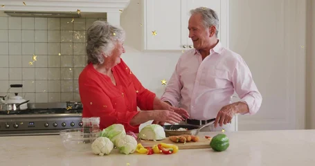 Selbstklebende Fototapeten Zu Kochen Chopping senior couple preparing meal in kitchen at island with vegetables, red blouse, pink shirt  © vectorfusionart