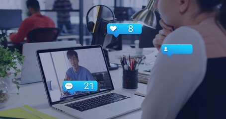 Watching woman at office desk resting chin, viewing laptop showing Korean in blue top, with bubbles