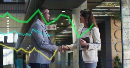 Shaking hands midadult business pros wearing blazers in office lobby, with tablet and data overlay