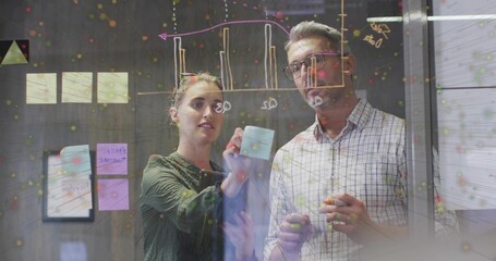 Placing woman in green blouse and man adding sticky notes on office glass wall, holding markers