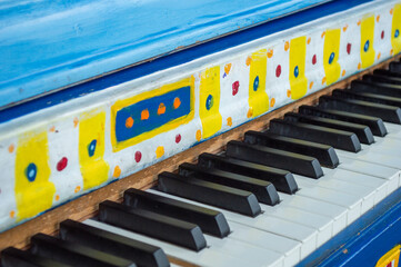 Close-up of a vibrant blue street piano with colorful hand-painted patterns on the fallboard, selective focus on black and white keyboard keys, public community music project and outdoor art.