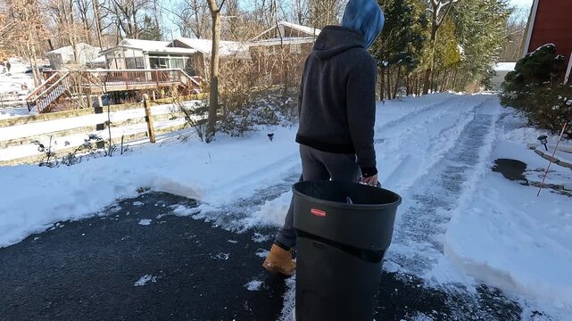 Berkeley Heights, NJ, USA - 01-30-2022: young man bringing the trash can down the driveway after snow storm in January in New Jersey