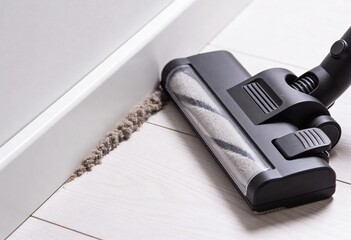 Close-up of a vacuum cleaner nozzle near a thick line of dust and dirt accumulation along a white skirting board.