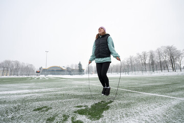 Girl jumps rope on a snowy football field in winter.