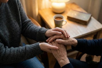 A close-up shot of a younger person's hands gently holding the aged hands of an older individual, conveying comfort and support in a warm indoor setting.